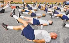  ?? AMY DAVIS/BALTIMORE SUN ?? A class of police trainees complete a morning exercise routine, including leg lifts, push-ups and sit-ups, at camp over the summer.