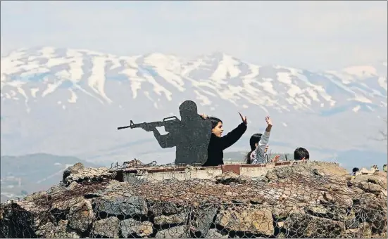  ?? JALAA MAREY / AFP ?? Unos niños saludando ayer junto a la silueta de un solado israelí en un puesto militar sobre el monte Bental, en los altos del Golán