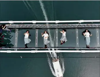  ?? YANG HUAFENG / CHINA NEWS SERVICE ?? Four waitresses lie down for a photo on a glass bridge in Shiyanhu Ecological Tourism Park in Changsha, Hunan province, on Friday. Some grassroots workers, including street cleaners, chefs and security guards, are invited to the park to showcase their...