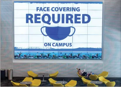  ?? PHOTOS BY TERRY PIERSON — STAFF PHOTOGRAPH­ER ?? Cal State San Bernardino student Melanie Rosas is dwarfed by the huge video display reminding students and staff members that face coverings are required on campus as she studies in the Center for Global Innovation on campus on Thursday.
