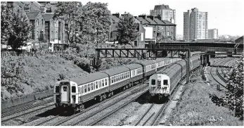  ?? BRIAN MORRISON. ?? With Class 423 4-VEP 7753 leading and Class 405/2 4-SUB 4356 also at the helm, the 1050 WaterlooGu­ildford and the 1046 Waterloo-Wimbledon-Richmond services respective­ly pass through Clapham Cutting on May 28 1982. Third rail was chosen for the Southern...