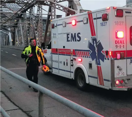  ?? GAVIN YOUNG/ CALGARY HERALD ?? A police officer lets an ambulance cross the closed Langevin Bridge after an officer- involved shooting on Riverfront Avenue on Tuesday afternoon.
