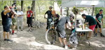  ?? Keith Bryant/The Weekly Vista ?? Mountain bikers stopped for refreshmen­ts, including bacon, beer and water, before tackling the last nine miles of the Ozark 25 ride Friday afternoon.