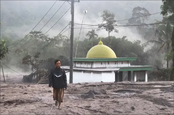  ?? Picture: AP Photo/imanuel Yoga ?? A man walks past a mosque partially covered in volcanic ash from the eruption of Mount Semeru in Kajar Kuning village in Lumajang, East Java. Indonesia’s highest volcano on its most densely populated island released searing gas clouds and rivers of lava Sunday in its latest eruption