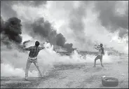  ?? AP/ADEL HANA ?? Palestinia­n protesters throw back tear-gas canisters at Israeli soldiers after they burned tires Friday near the fence at the Gaza Strip’s border with Israel.