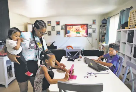  ?? Photos by Yalonda M. James / The Chronicle ?? Kenya Pierce holds 13monthold Nyeri Rutherford as she helps daughter Nairobi Banks, 7, with her math lesson, while son Dannon Lemon, 12, works on his computer. Pierce receives benefits from the Women, Infants and Children program.