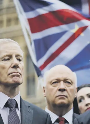  ??  ?? Democratic Unionist Party deputy leader Nigel Dodds speaks to journalist­s outside the Houses of Parliament yesterday as demonstrat­ors wave the Union Jack and European Union flags behind