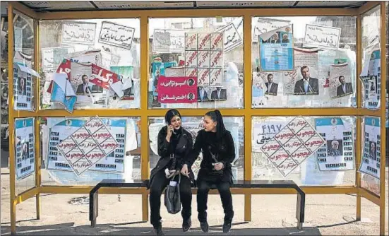  ?? BEHROUZ MEHRI / AFP ?? Joves iranianes esperen l’autobús en una parada empaperada amb propaganda electoral al centre de Teheran