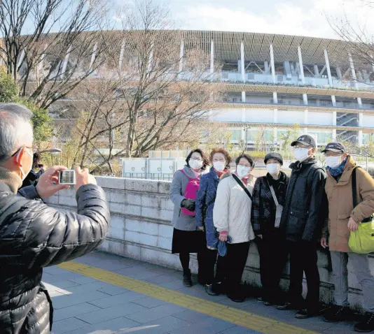  ?? FILE ?? Tourists wear masks to prevent the spread of COVID-19 as they pause recently for photos against the New National Stadium, a venue for the opening and closing ceremonies at the Tokyo 2021 Olympics.