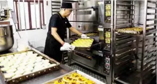  ??  ?? Chef Dennis del Rosario turning a tray of egg tarts to make sure they cook evenly at Lord Stow’s bakery in Macau. — AFP photos