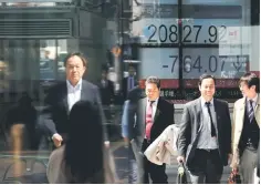  ??  ?? People walk past an electronic board showing Japan’s Nikkei average outside a brokerage in Tokyo, March 23. As US President Donald Trump dealt a blow to China with plans to slap tariffs on US$60 billion of trade, he quietly delivered a slap in the face...