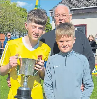  ??  ?? Ferry Athletic U/16 captain Greg Breen receives the John Clark Motors Cup from DDYFA official Colin “Chippy” Lowe and his grandson Rhys Garmany.