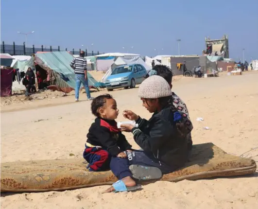  ?? ?? ► Una niña palestina desplazada, que huyó de su casa debido a los ataques israelíes, alimenta a su hermano en un campamento.