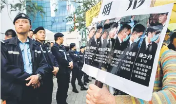  ??  ?? Police (left) stand guard as pro-democracy supporters (right) chant slogans and hold placards after the arrival of the seven police officers (pictured in placard on right), who were found guilty outside the District Court in Hong Kong. — AFP photo