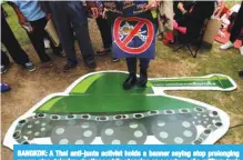  ?? —AFP ?? BANGKOK: A Thai anti-junta activist holds a banner saying stop prolonging power, stop delaying elections while stepping on a cartoon of a military tank during a pro-democracy rally at a university field.