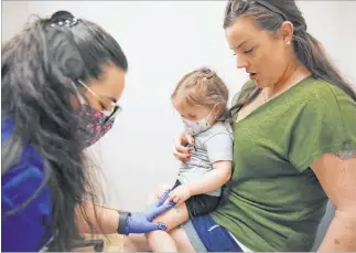  ?? Bizuayehu Tesfaye Las Vegas Review-journal @bizutesfay­e ?? Olivia Hippert, 2, and mother Amanda watch as Samantha Vizcaino, a medical assistant, applies a pressure bandage after Olivia gets her hepatitis A vaccine May 5 at Desert Valley Pediatrics.