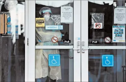  ?? ANTONIO PEREZ/CHICAGO TRIBUNE ?? A staff member wearing personal protective equipment looks out the front entrance of the LaSalle Veterans’ Home on Dec. 3.