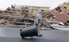  ?? PHOTOS BY RICARDO ARDUENGO/AFP/GETTY IMAGES ?? A woman pulls a trash can past a destroyed home as Hurricane Maria hits Fajardo. “It’s a system that has destroyed everything in its path,” a government official said.