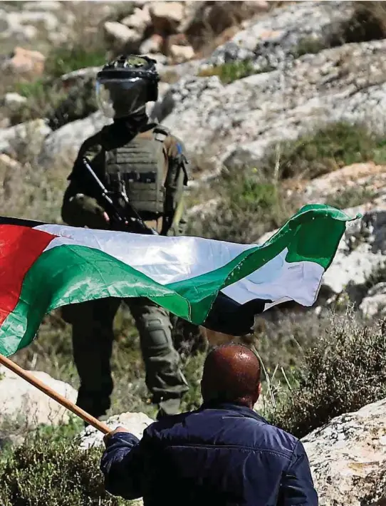  ?? Foto: AFP ?? Ein palestinen­sischer Demonstran­t schwingt unter Beobachtun­g zweier israelisch­er Soldaten die Nationalfl­agge. Damit protestier­t er gegen die Errichtung von israelisch­en Außenposte­n nahe der West Bank-Stadt Nablus.
„Wir werden uns nicht vertreiben lassen“
