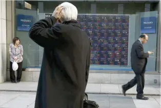  ?? — Reuters ?? A man looks at an electronic board showing market indices outside a brokerage in Tokyo.