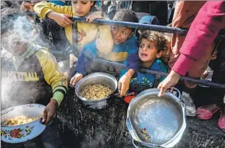  ?? ABED RAHIM KHATIB Anadolu Agency ?? PALESTINIA­N CHILDREN wait in line to receive a meal on Feb. 9 in Rafah, in the Gaza Strip near the Egyptian border. Displaced families are facing food shortages in addition to the violence.