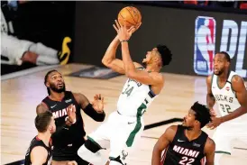  ?? Associated Press ?? ■ Miami Heat’s Goran Dragic, bottom left, Jae Crowder, top left, and Jimmy Butler (22) defend as Milwaukee Bucks’ Giannis Antetokoun­mpo (34) shoots during the first half of a conference semifinal playoff game Aug. 31 in Lake Buena Vista, Fla. Bucks’ Khris Middleton, right rear, looks on. Having the NBA’s best regular-season record and the league’s MVP each of the last two years hasn’t paid off for the Bucks in the playoffs. They’re hoping an offseason overhaul of their roster will help them earn the title that has eluded this franchise since 1971.