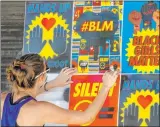  ?? L.E. Baskow Las Vegas Review-journal @Left_eye_images ?? Cynthia Hartness attaches posters Friday to the facade of the Majestic Repertory Theatre building during a mural project by experienti­al company Good All Day Collective for Juneteenth.