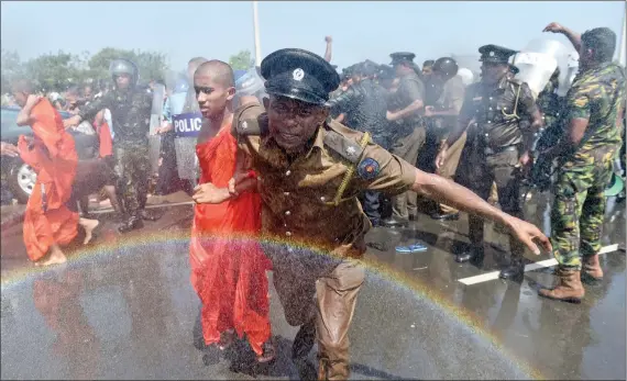  ?? AFP ?? MONKS AGAINST CHINA IN LANKA: A Sri Lankan policeman leads a monk from a protest in the southern port city of Hambantota on Saturday. Sri Lankan nationalis­ts, monks and local residents are protesting the creation of an industrial zone for Chinese investment­s on the island.