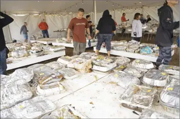  ?? The Maui News / COLLEEN UECHI photos ?? Keoni Sithar (center, in red) surveys the dozens of color-coded pans of turkey and other meats awaiting pickup by community members.