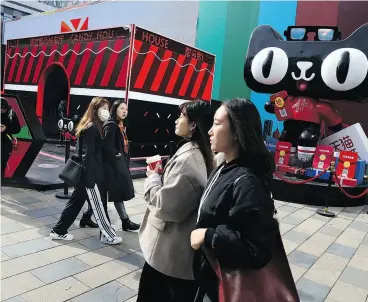  ?? NG HAN GUAN / THE ASSOCIATED PRESS ?? Beijing shoppers walk by an Alibaba promotion for the upcoming Singles Day event. Begun in the ’90s as a version of Valentine’s Day for people without romantic partners to splurge on themselves, the day has grown into the world’s biggest e-commerce event.