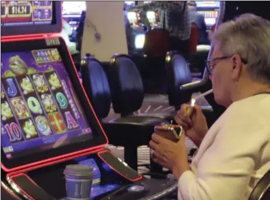  ?? (AP/Wayne Parry) ?? A gambler lights a cigarette at a slot machine in Harrah’s casino in Atlantic City, N.J., in late September.