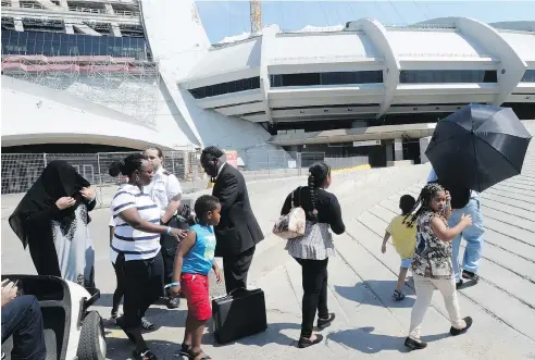  ?? RYAN REMIORZ / THE CANADIAN PRESS ?? Asylum seekers take a walk outside Olympic Stadium as security guards look on in Montreal on Wednesday. The stadium will be housing asylum seekers after a spike in the number of people crossing at the United States border in recent months.