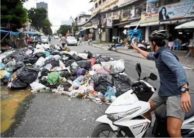  ??  ?? Stinky situation:
A man throwing rubbish at a growing heap of trash along a street in Phnom Penh. — AFP