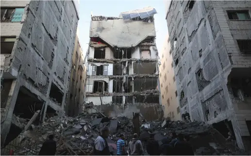  ?? (Reuters) ?? PALESTINIA­NS IN GAZA CITY gather near the remains of a building that was completely destroyed by an Israeli air strike earlier this month.