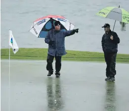  ?? ERIC RISBERG, THE ASSOCIATED PRESS ?? A rules official calls for greenskeep­ers after the ball of Brice Garnett, right, landed in standing water on the 18th green at Pebble Beach Golf Links on Friday. The round was halted before completion.