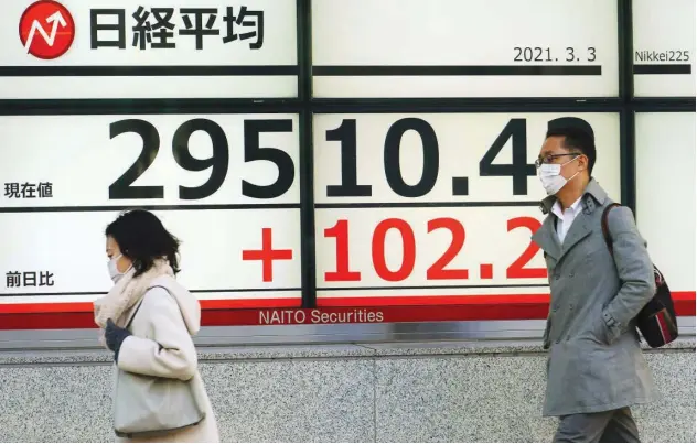  ?? Associated Press ?? ↑
People walk past a stock board of a securities firm in Tokyo on Wednesday.