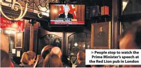  ??  ?? &gt; People stop to watch the Prime Minister’s speech at the Red Lion pub in London