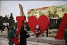  ?? HASSAN AMMAR - THE ASSOCIATED PRESS ?? A Syrian woman uses her mobile phone Jan. 19 to take a picture of her daughter in front of a huge banner showing Syrian President Bashar Assad as others gather at Saadallah al-Jabiri Square in Aleppo, Syria. Thirteen months after government forces...