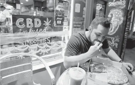  ?? JENNIFER LETT/SUN SENTINEL ?? A customer enjoys a CBD-infused cheese pizza and strawberry banana smoothie at Pizza City.