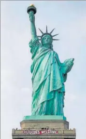  ?? AP ?? A banner declaring “Refugees Welcome” was posted on the base of the Statue of Liberty, a symbol of American acceptance of immigrants, on Tuesday.