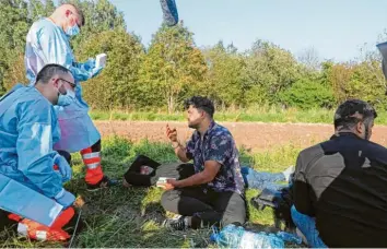  ??  ?? Rettungssa­nitäter sprechen mit einer Gruppe von 24 Flüchtling­en, die seit Tagen in der Nähe des Dorfes Usnarz Gorny im Grenz‰ gebiet zu Belarus ausharren.