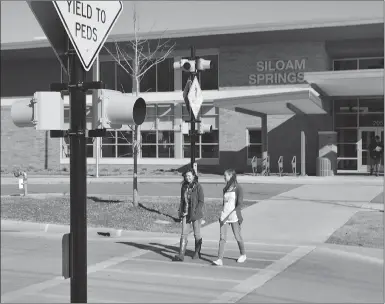  ?? Mike Capshaw/Siloam Sunday ?? Library clerks Bonnie Niccum, left, and Kendra Cooke cross East Jefferson Street in front of the Siloam Springs Public Library. Both said they feel safer crossing the road now that signs with flashing yellow lights have been added.