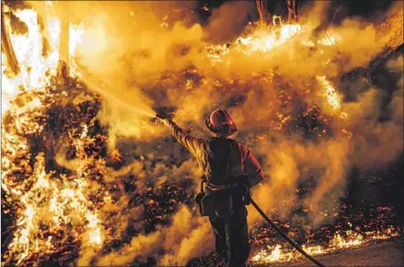  ?? Marcus Yam Los Angeles Times ?? A FIREFIGHTE­R sprays water on a back fire as the Maria fire moves toward Santa Paula on Friday. The fire’s cause isn’t known.
