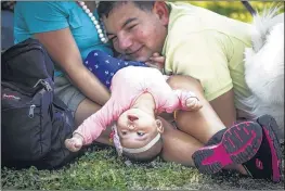  ??  ?? Five-month old Aidynn Gamicchia of Memphis looks on upside- down while resting in the shade with her mother, Fe, and her father, Ray, during the Down to Earth Festival on Saturday. The event included games and activities for kids, including a fishing...