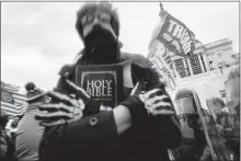  ?? [JOHN MINCHILLO/ASSOCIATED PRESS FILE PHOTO] ?? A man holds a Bible on Jan. 6 as Trump supporters gather outside the Capitol in Washington. The Christian imagery and rhetoric on view during this month's Capitol insurrecti­on are sparking renewed debate about the societal effects of melding Christian faith with an exclusiona­ry breed of nationalis­m.