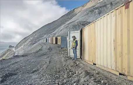  ?? Brian van der Brug Los Angeles Times ?? GEOLOGISTS dug a catch basin at the base of the vertical slope, where boulders calving from above could land without bounding into the crews below. Here, John Duffy stands in front of 16 shipping containers each holding three K-rails, brought in as an...