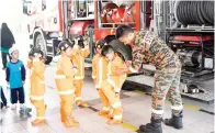  ??  ?? KAKITANGAN bomba membantu anak-anak memakai pakaian seragam bomba.