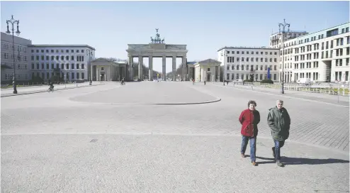  ?? ODD ANDERSEN / AFP via Gett y Imag es ?? An couple walks across the deserted Pariser Platz by the Brandenbur­g Gate in Berlin on Monday.