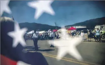  ?? Francine Orr Los Angeles Times ?? AT TOP, STREET signs partly melted by the heat of last year’s Dixie fire in Greenville, Calif. Bottom, the start of the Sierra Nevada town’s traditiona­l Gold Diggers Day parade is visible through an American flag.