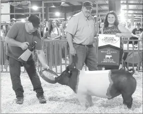  ?? Westside Eagle Observer/SUBMITTED ?? Paige Barrett (right) receives a Grand Champion banner from judge Brian Anderson (center) after winning the Benton County Youth Livestock show’s Grand Champion Market hog award at the Benton County Fair in Bentonvill­e on Aug. 11, 2017.